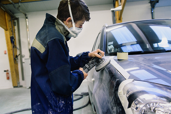 Un artisan en blouse bleue appliquant de la peinture sur une carrosserie de voiture à Fès.